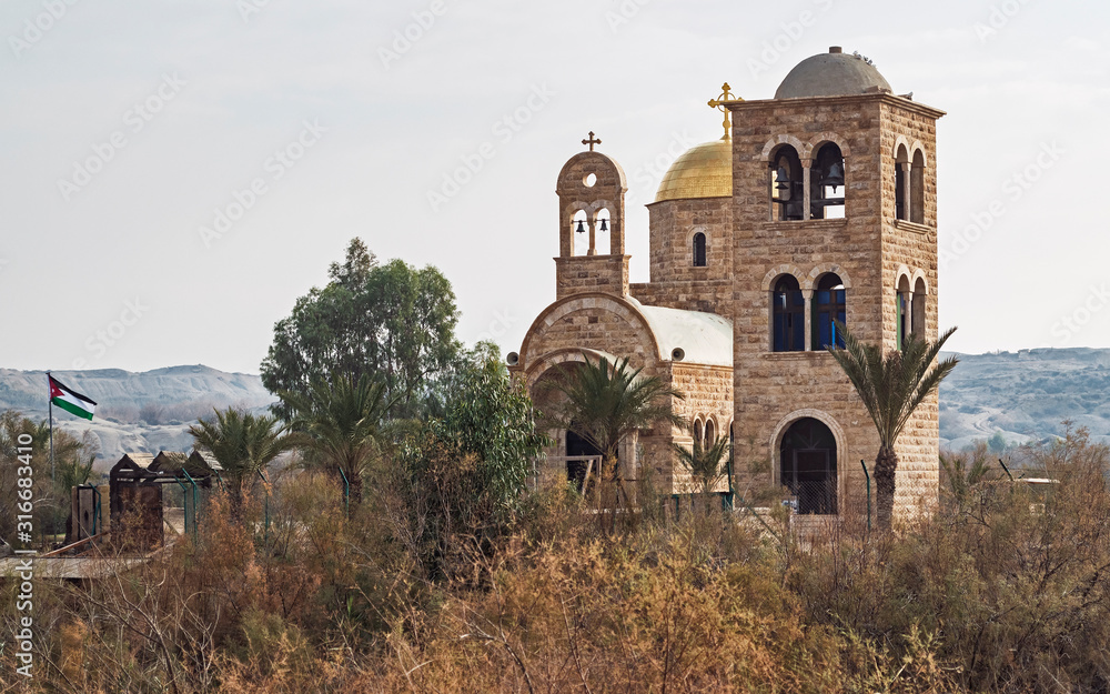 ancient and modern stone churches at the site of the baptism of jesus on the jordan river viewed from the west bank