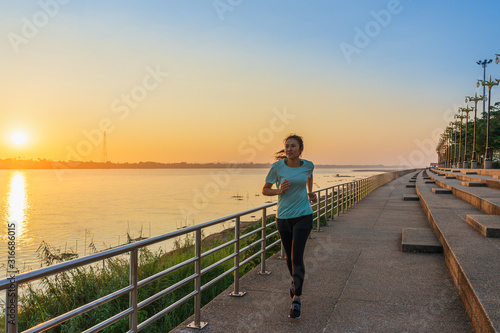Young fitness Asian woman is running and jogging an outdoor workout on the riverwalk in the morning for lifestyle health.
