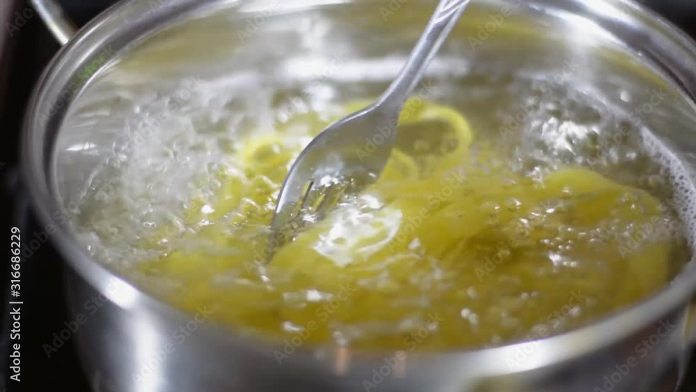 stirs the pasta with a fork in a pot of boiling water. stirs the pasta with a fork in a pot of boiling water.