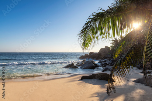 Sunset at exotic tropical beach with coco palms and turquoise sea in exotic Paradise island.