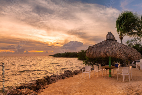 Tropical sandy beach at sunset with coco palms and beach umbrella with chairs in Key West  Florida.