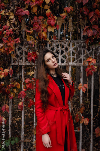 Beautiful young woman in red coat is enjoying autumn park.