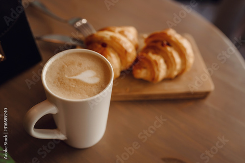 Cappuccino with beautiful latte art and croissant on wooden background