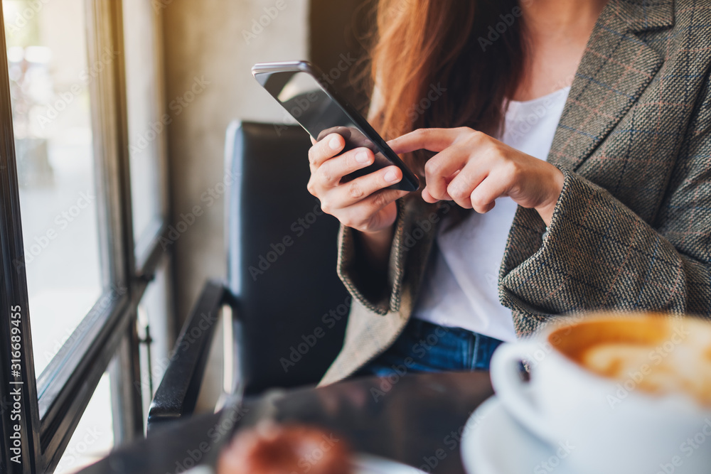 Closeup image of an asian woman holding and using mobile phone with coffee cup on the table in cafe Closeup image of an asian woman holding and using mobile phone with coffee cup on the table in cafe