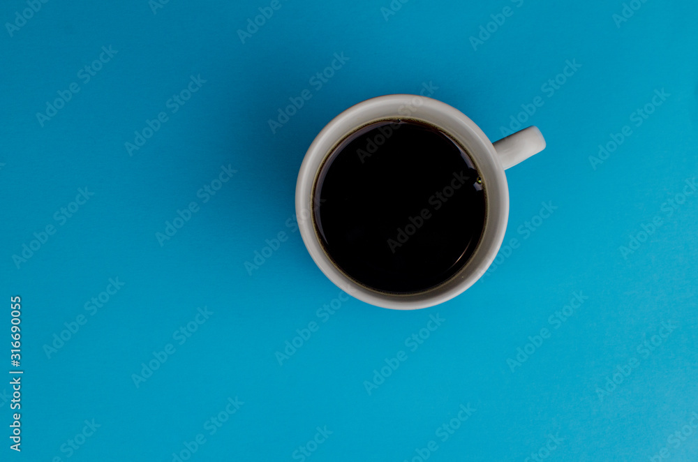 A cup of fresh coffee on blue background with text space. Flat lay. Top view. Minimalism A cup of fresh coffee on blue background with text space. Flat lay. Top view. Minimalism