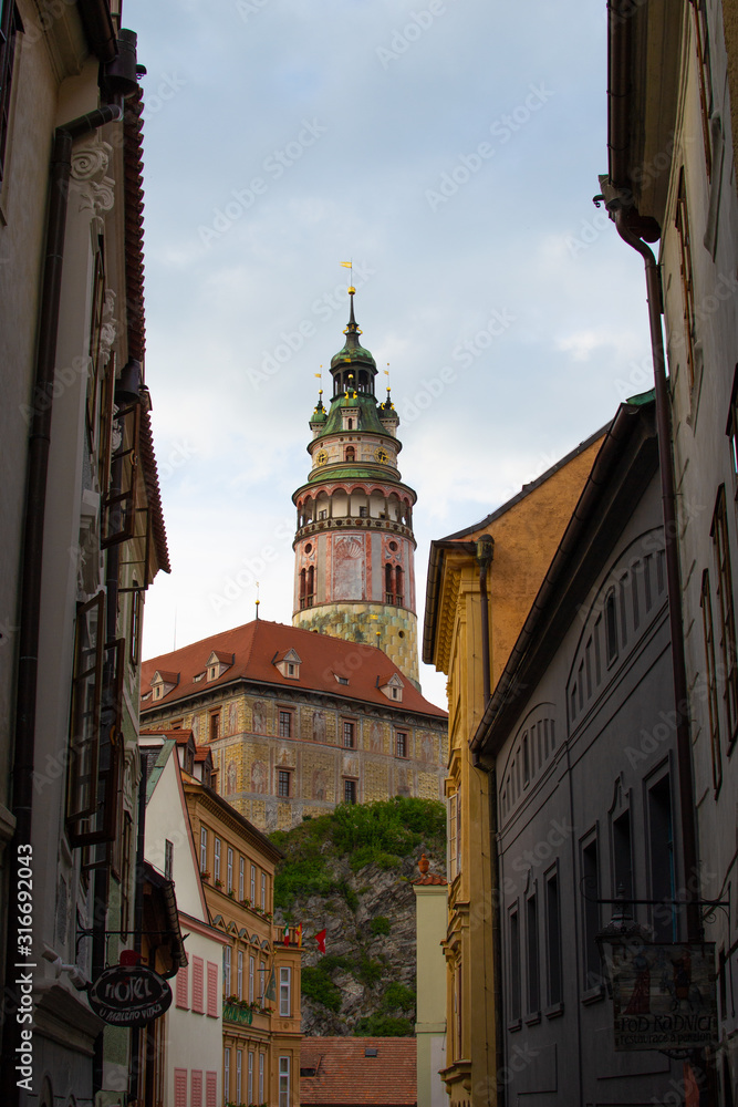 Fototapeta premium Vertical picture of the Castle Tower, the most famous symbol of Cesky Krumlov, in State Castle, viewed between some buildings (Czech Republic)