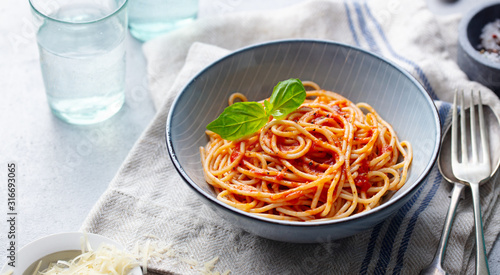 Pasta, spaghetti with tomato sauce and fresh basil in a bowl. Grey background. Copy space.