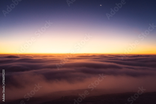 Winter landscape in Krkonose, beautiful sunrise with moon above the heavy clouds, shot from highest mountain in Czech republic called Snezka. © Tomas