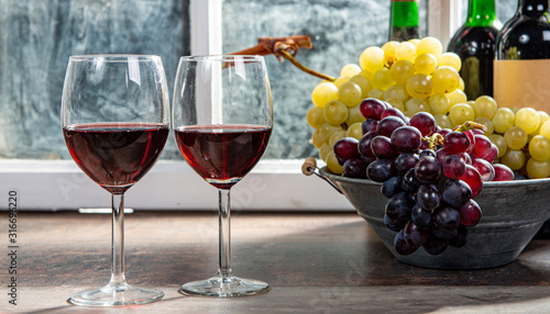 two wineglasses, red and white grapes with bottles of red wine