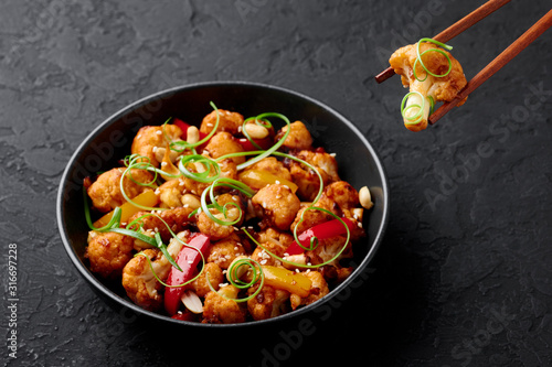 Kung Pao Cauliflower at dark slate background. Sichuan Kung Pao Cauliflower is chinese cuisine vegetarian dish with chilli peppers, peanuts, sauces and onion.