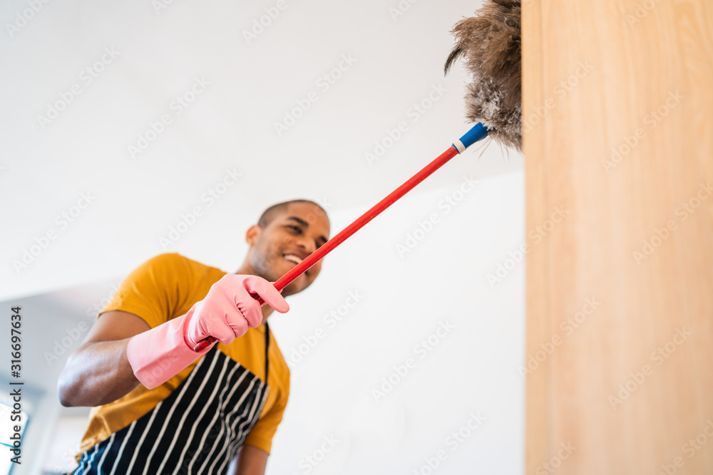 Young latin man dusting his new house.