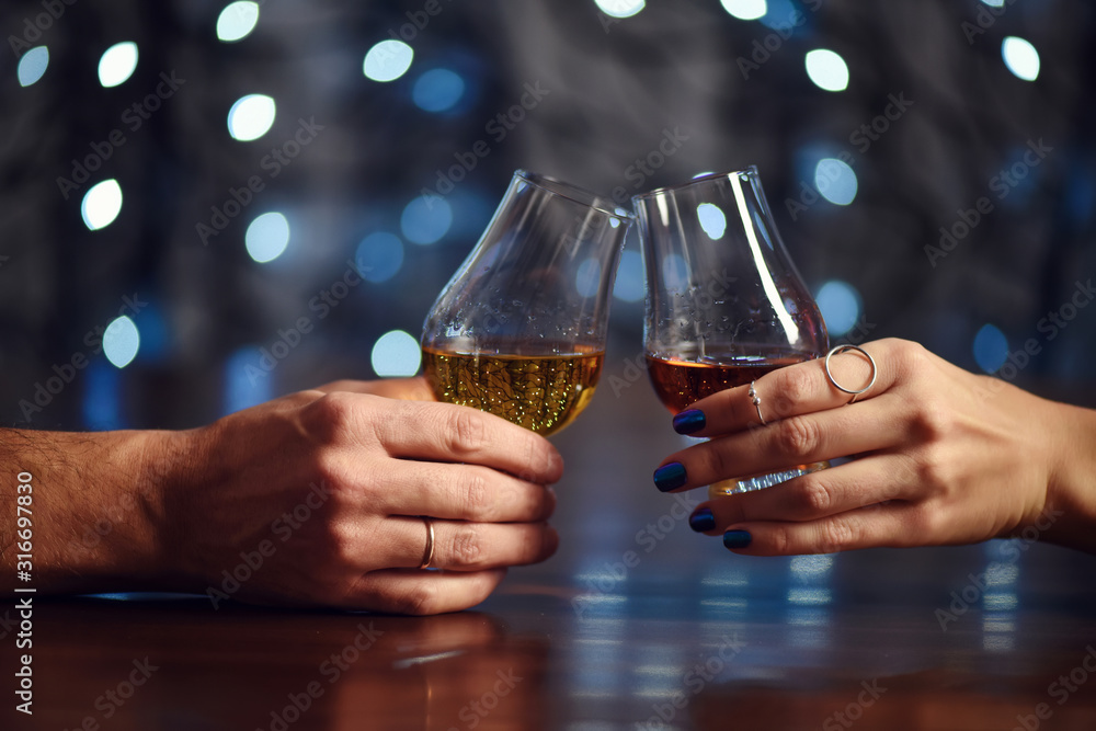 A couple makes a toast with two glasses of whiskey on festive background