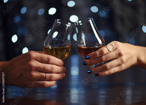 A couple makes a toast with two glasses of whiskey on festive background