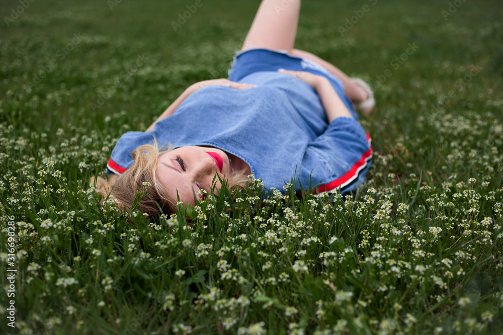 Unity with the nature of the pregnant woman, female lies on spring grass in peach flower garden. The model wearing denim dress . Unity with the nature of the pregnant woman, female lies on spring grass in peach flower garden. The model wearing denim dress .