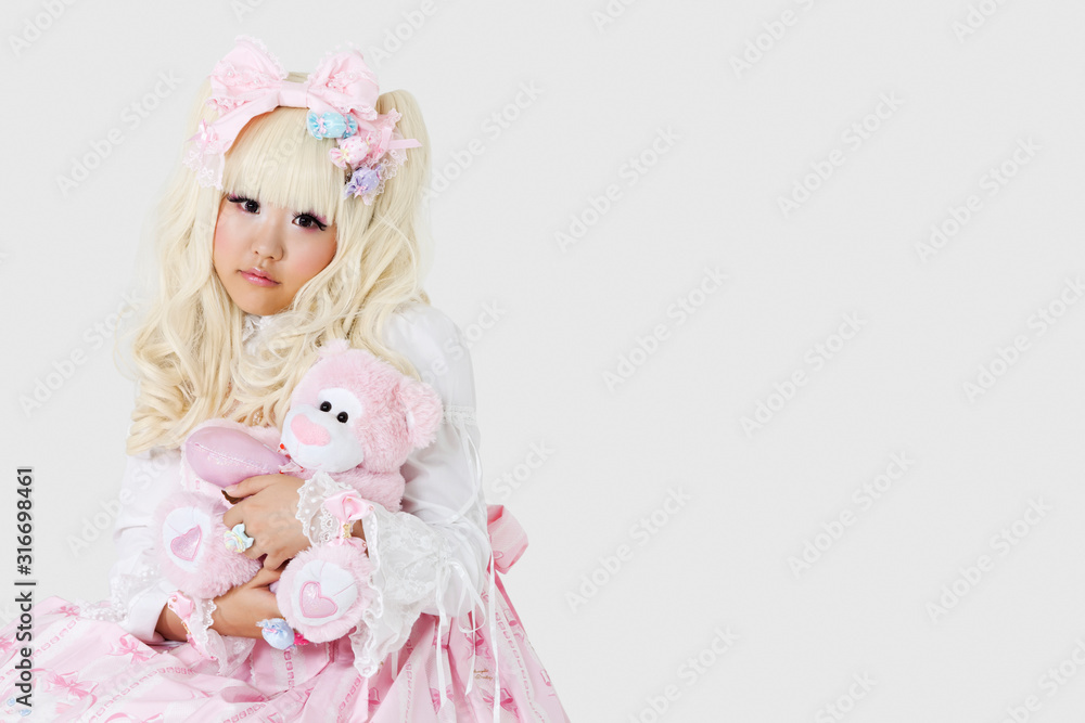 Fototapeta premium Portrait of cute woman dressed as a doll holding soft toy over gray background