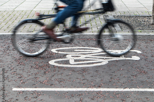 Painted cycle path bicycle sign on the ground with a rider passing.  Motion blurr on the bike and rider.