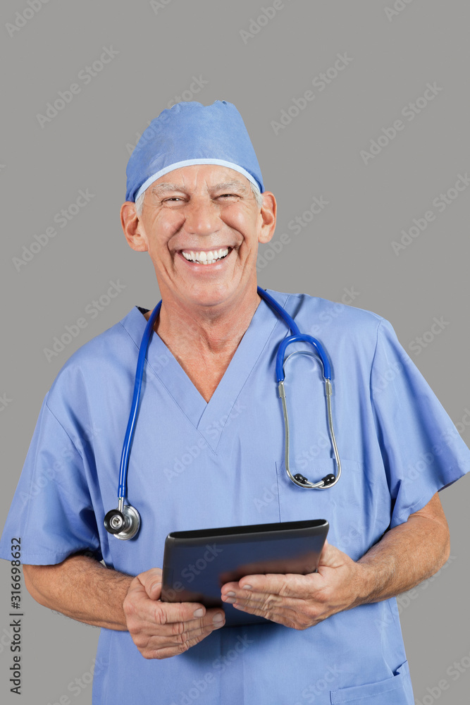 Portrait of senior male surgeon holding tablet PC over gray background Portrait of senior male surgeon holding tablet PC over gray background