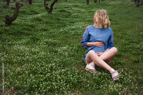 Unity with the nature of the pregnant woman,  femaie sit on spring grass in peach flower garden. The model wearing denim dress . The dream of future motherhood is beautiful for morher photo