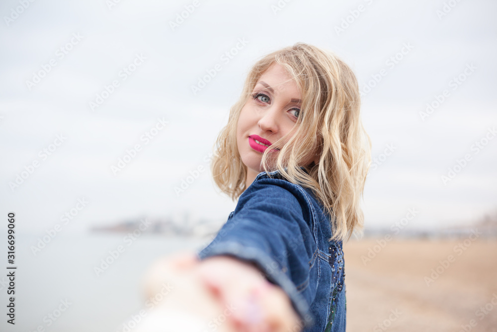 Blond woman holding male hand and look to camera. The female walk in the shore of the sea and think about the silence of a deserted beach Blond woman holding male hand and look to camera. The female walk in the shore of the sea and think about the silence of a deserted beach