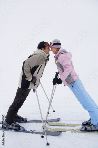 Couple leaning towards each other standing on skis side view