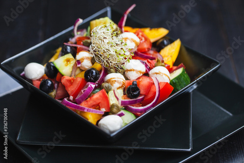 salad with tomato, cucumber, olives, bell pepper, onions and baby mozzarella in a plate