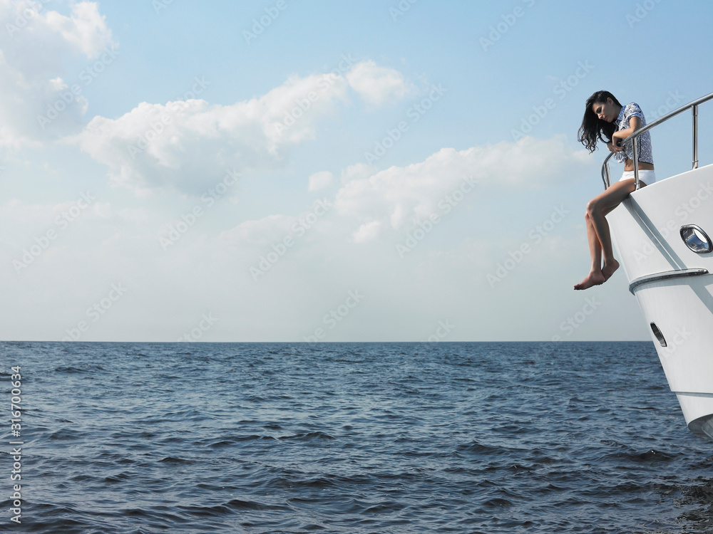 Young woman sitting at edge of yacht with legs dangling overboard side view Young woman sitting at edge of yacht with legs dangling overboard side view