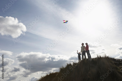 Silhouette of parents and child flying kite on dunes