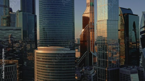 Aerial drone zoom out circular center of Moscow city buildings, skyscrapers during sunset. Drone shot flying over Moscow skyscrapers in summer evening