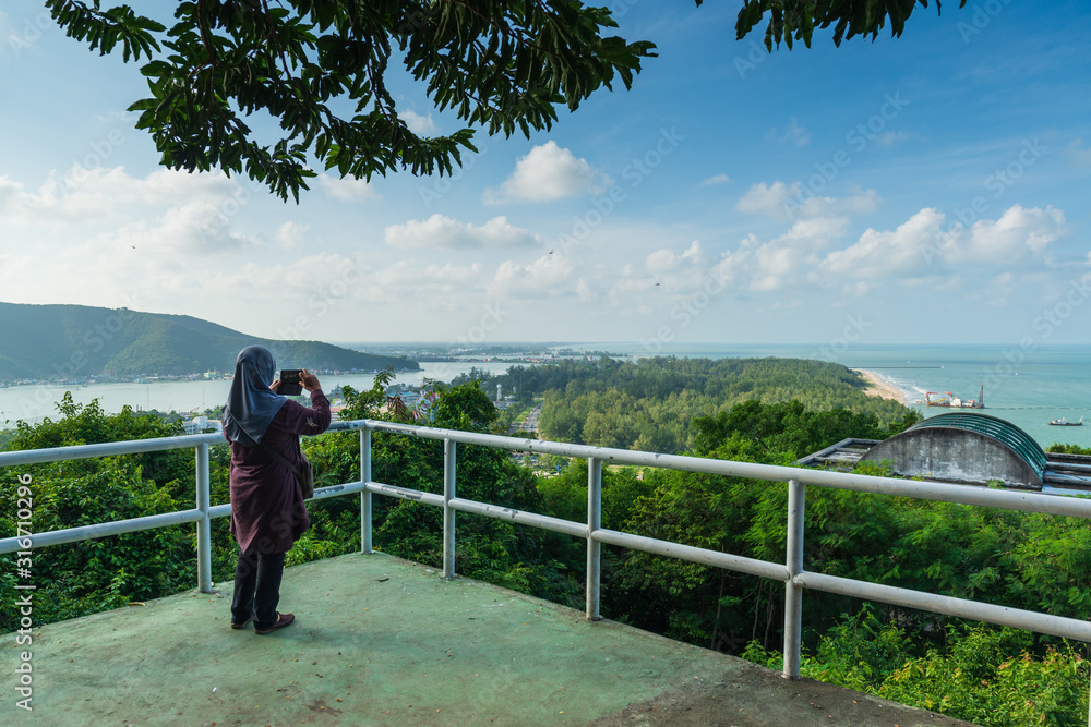 Unidentified muslim woman is lifting the mobile phone to take a photo at viewpoint on the top of Khao Tang Kuan, Songkhla, Thailand... .