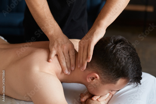 Young man enjoying back and shouders massage in spa.Professional massage therapist is treating a male patient in apartment.Relaxation,beauty,body and face treatment concept.Home massage.