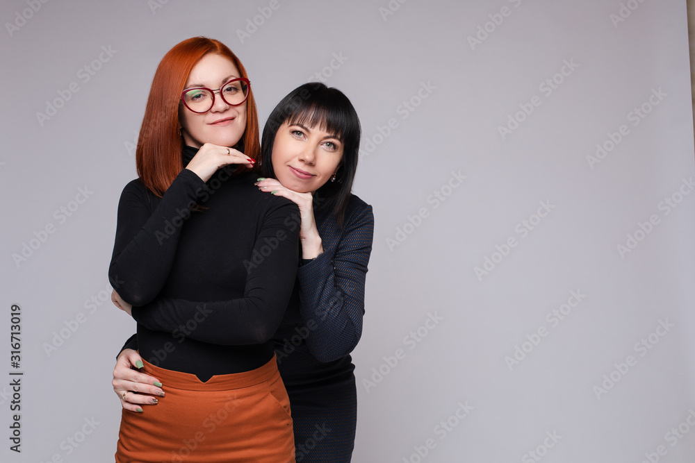 Stock photo of attractive women with red and dark hair posing snuggling at camera. Dark-haired woman embracing her friend from behind. Stock photo of attractive women with red and dark hair posing snuggling at camera. Dark-haired woman embracing her friend from behind.