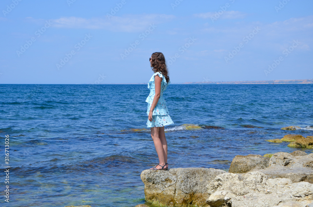 Young woman in a dress on a rocky seashore on a summer day
