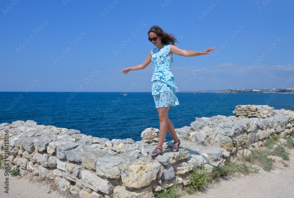 Young woman in a dress on a rocky seashore on a summer day
