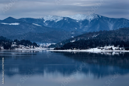 Frozen lake and pine trees in snow at Colibita. Romania early morning winter scen.