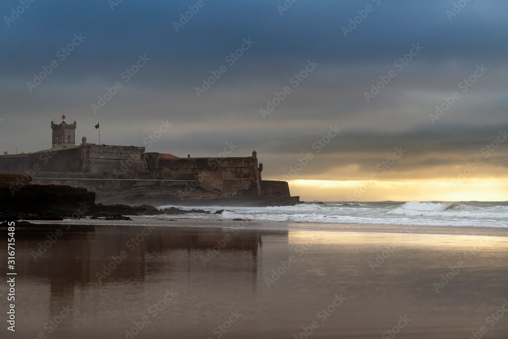 View of the Carcavelos Beach with the Sao Juliao da Barra Fort on the background at sunrise, in Portugal.
