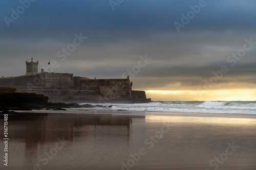 View of the Carcavelos Beach with the Sao Juliao da Barra Fort on the background at sunrise, in Portugal.