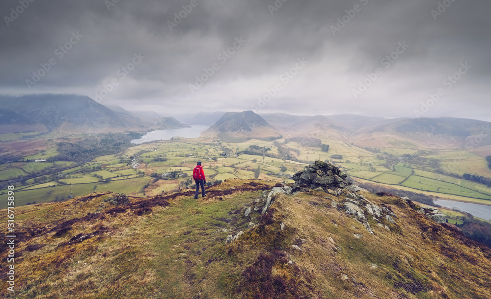 A hiker walking down from the mountain summit of Bield with views of Loweswater and Crmmock Water in the distance.