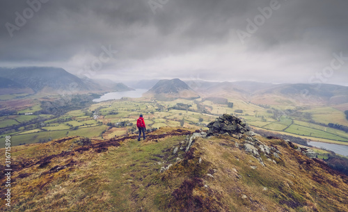 A hiker walking down from the mountain summit of Bield with views of Loweswater and Crmmock Water in the distance.