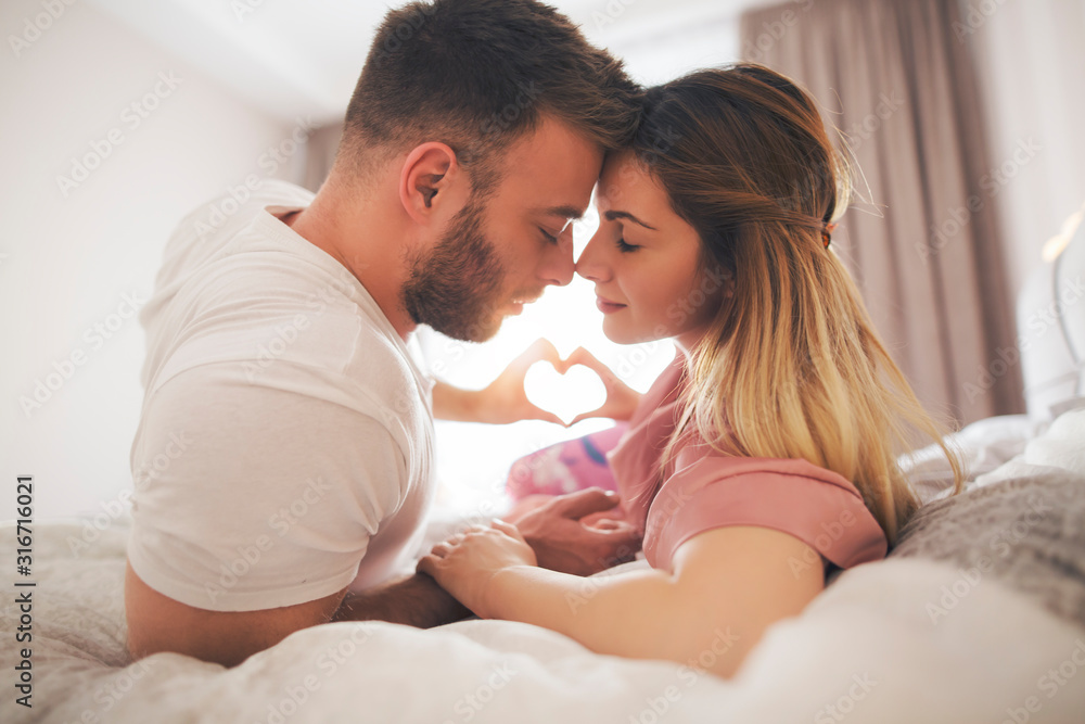 Beautiful couple in bed showing heart symbol with their hands. Beautiful couple in bed showing heart symbol with their hands.