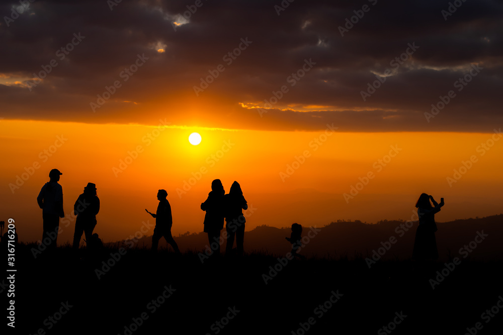 Group of silhouette people on top of a mountain on sunset.