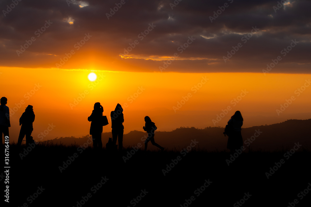 Group of silhouette people on top of a mountain on sunset.