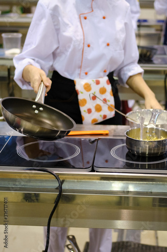 Woman chef roasts in a frying pan in the hotel's public kitchen