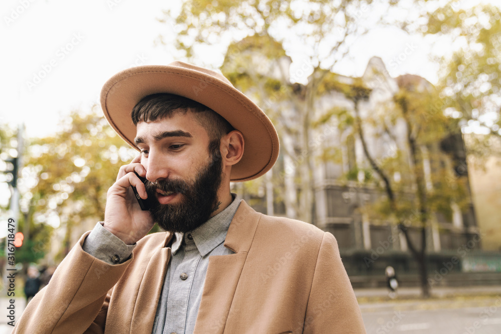 Image of stylish young man talking on cellphone while walking outdoors Image of stylish young man talking on cellphone while walking outdoors