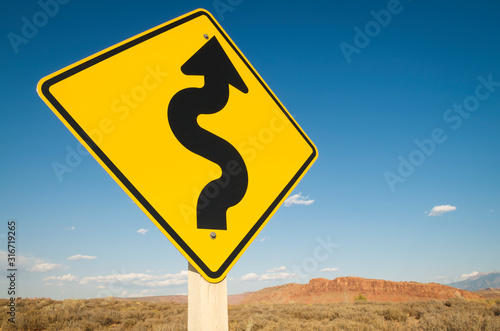 Black curving arrow on bright yellow roadsign pointing ahead to stark desert landscape