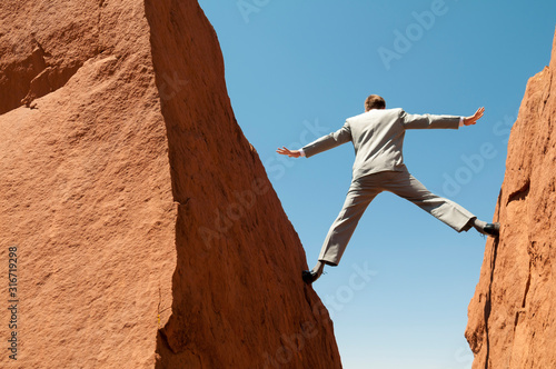 Unrecognizable businessman balancing outdoors between two jagged rocks forming a deep crevasse against blue sky photo