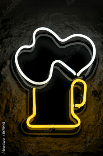 Big frothy mug of beer in bright neon against dark night background 