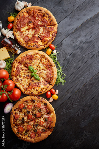 Wallpaper Mural Freshly served, three various pizzas placed among tasty ingredients. Top view Torontodigital.ca