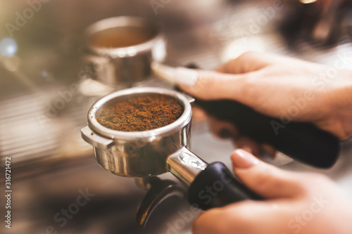 Barista woman holding coffee holder with ground coffee near professional coffee machine close up