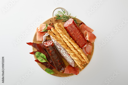 top view of delicious meat platter served with breadsticks and herbs on board isolated on white