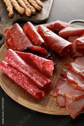 delicious meat platter on wooden board on black surface